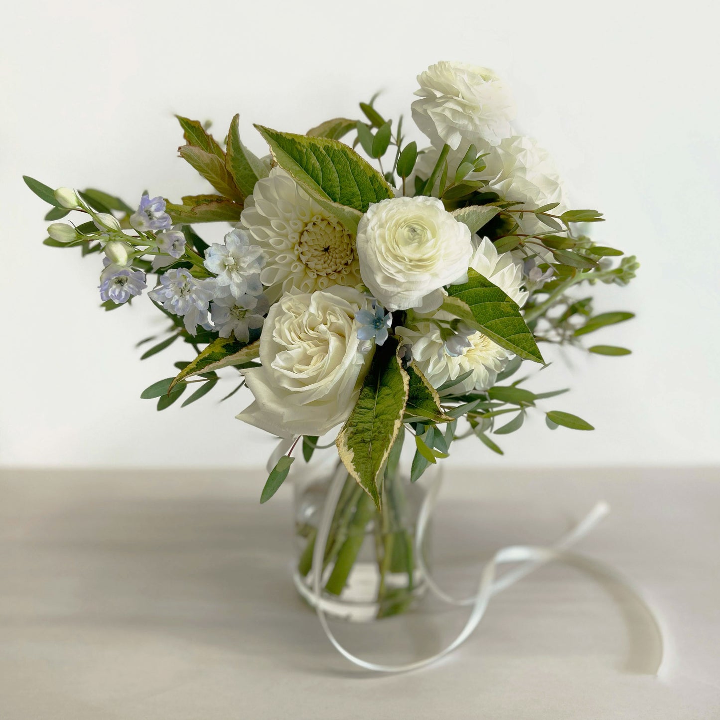 Full shot, Soft whites, peaches, and light blue flowers. Attendant bouquet, bridesmaid bouquet, posy-style bouquets for bridesmaids. They emphasize blooms over greenery, are hand-tied & finished with a ribbon of your choice, and come in a vase. From the best wedding florist in Toronto Quince Flowers.