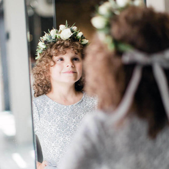 The image showcases a person’s head adorned with a beautiful arrangement of flowers and leaves, creating a natural and elegant look. The individual has dark, curly hair that provides a contrasting backdrop to the vibrant colors of the foliage and blossoms intertwined within it. The setting appears to be outdoors, surrounded by greenery. Order online for wedding & event flowers from the best florist in Toronto near you.