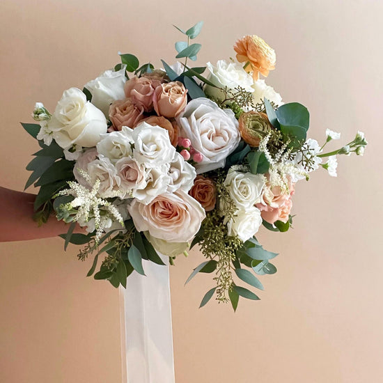 Beautiful bridal bouquet of assorted flowers including roses and poppies, adorned with a white ribbon, against a plain white background. Order online for wedding & event flowers from the best florist in Toronto near you.