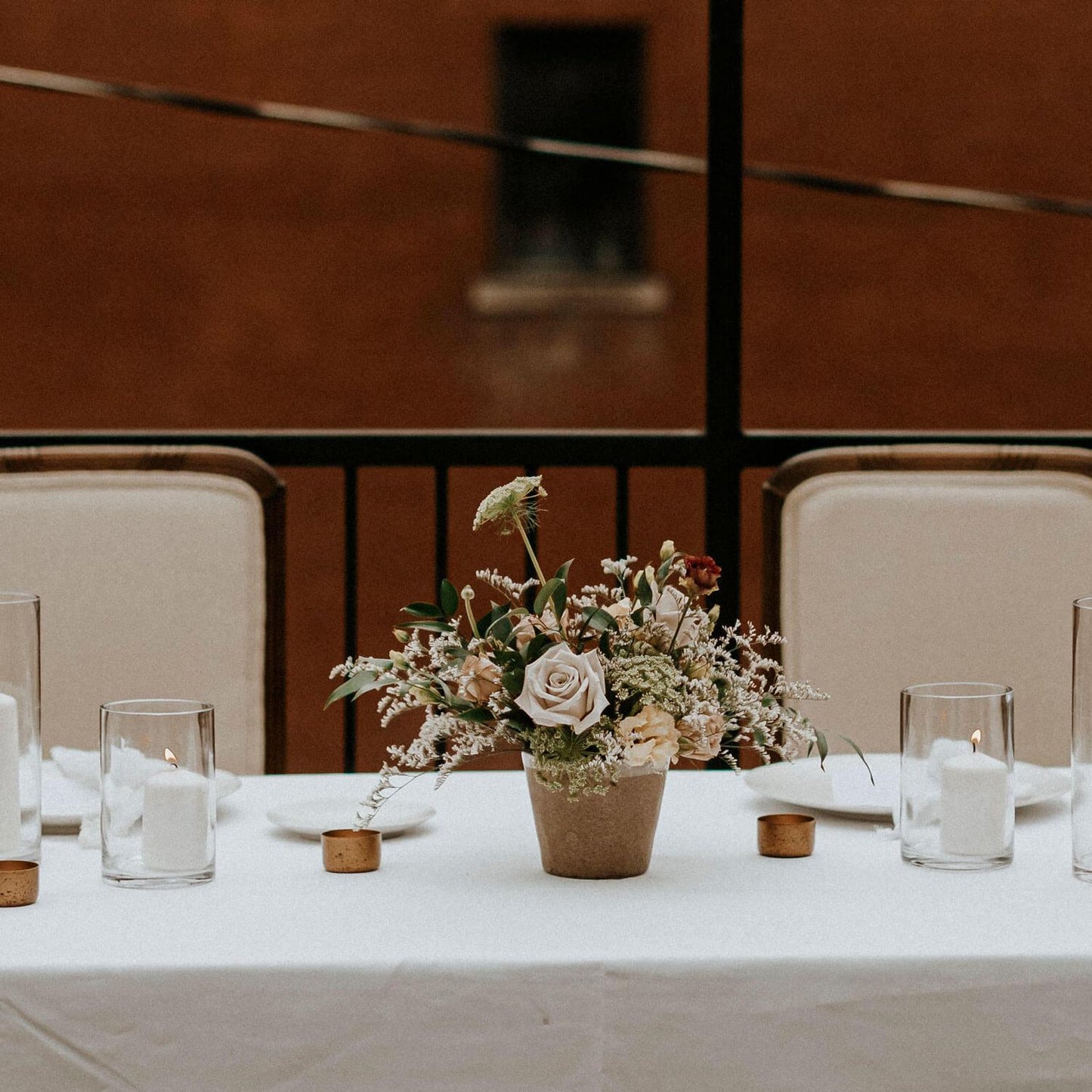 A table setting with a floral centerpiece, candles, and chairs in an indoor environment. Order online for wedding & event flowers from the best florist in Toronto near you.