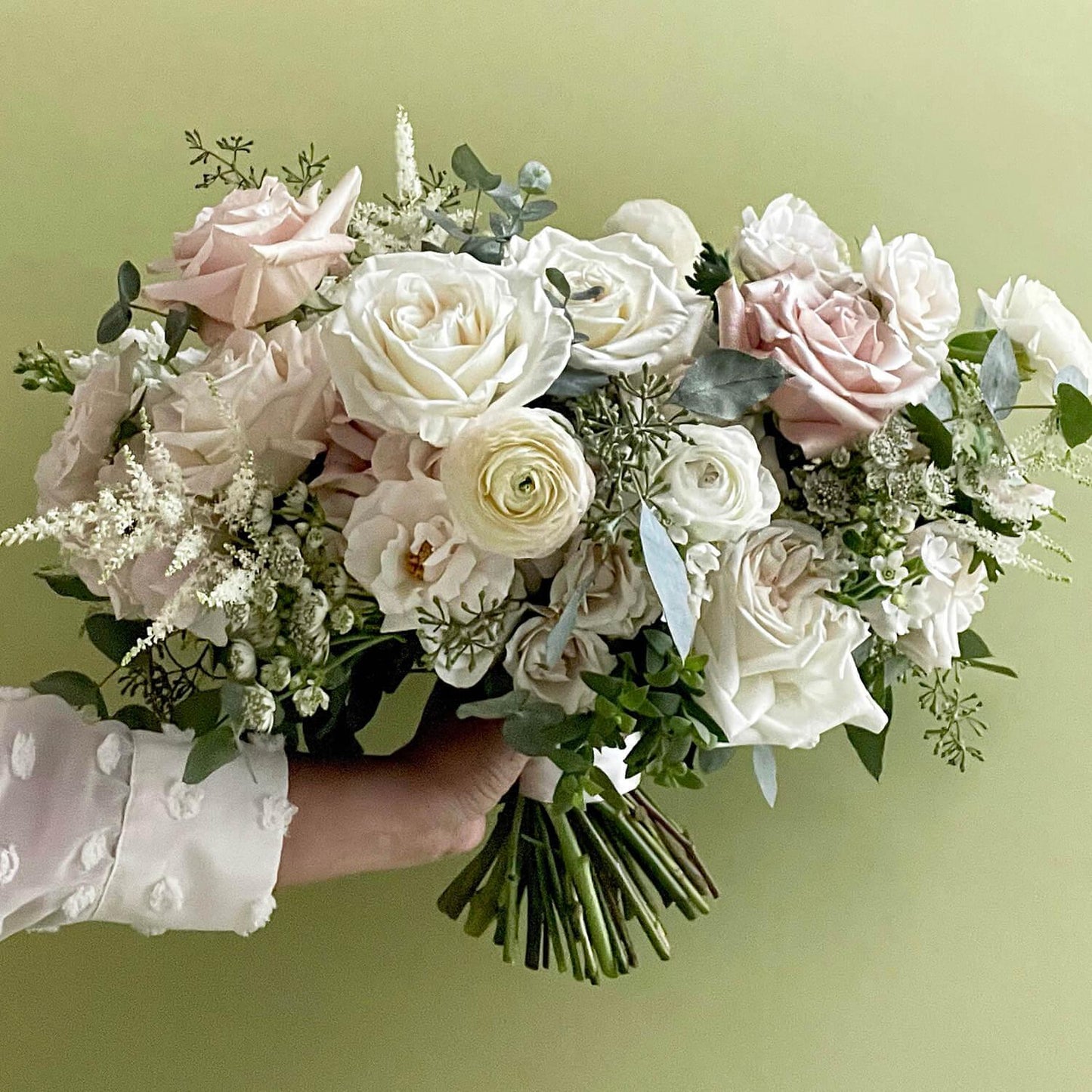 Beautiful bridal bouquet of assorted flowers including roses and poppies, adorned with a white ribbon, against a plain white background. Our bouquets marry creative vision and nature. We work with luxurious flower varieties including garden roses, dahlias, and peonies in season. They emphasize blooms over greenery, are hand-tied & finished with a ribbon of your choice, and come in a vase. From the best wedding florist in Toronto Quince Flowers.