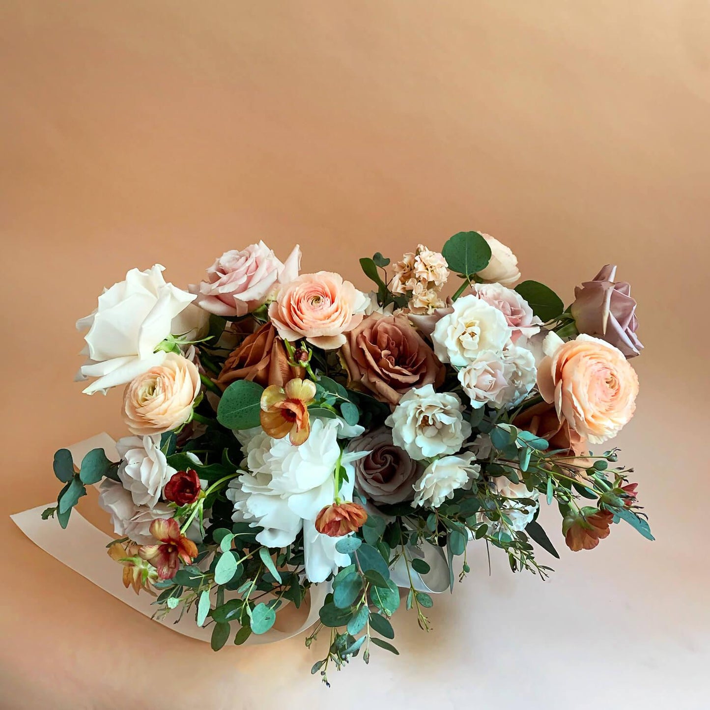 Beautiful bridal bouquet of assorted flowers including roses and poppies, adorned with a white ribbon, against a plain white background. Our bouquets marry creative vision and nature. We work with luxurious flower varieties including garden roses, dahlias, and peonies in season. They emphasize blooms over greenery, are hand-tied & finished with a ribbon of your choice, and come in a vase. From the best wedding florist in Toronto Quince Flowers.