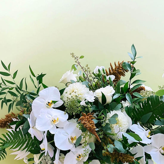 A bouquet of various white flowers and green foliage against a pale background. Order online for sympathy & event flowers from the best florist in Toronto near you.