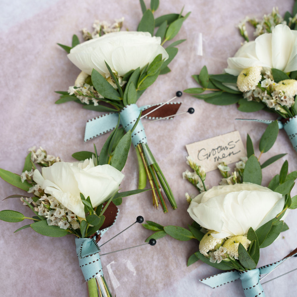 Closeup of white flower Boutonnieres for the groomsmen – Worn on the lapel of a tuxedo or suit jacket, boutonnieres or “buttonhole” flowers, typically use a single blossom, foliage, and textured elements, finished with ribbon. From the best wedding florist in Toronto Quince Flowers.