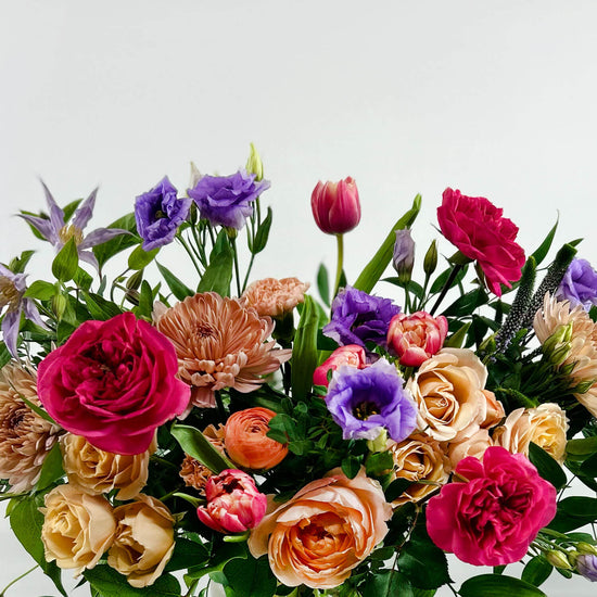 Close-up image of a funny valentines day bouquet with lavender lisianthus, blue clematis, pink, peach, and apricot garden roses, double tulips, apricot ranunculus, and carnations. Order online for same-day flower delivery from Toronto's best florist, available near you.