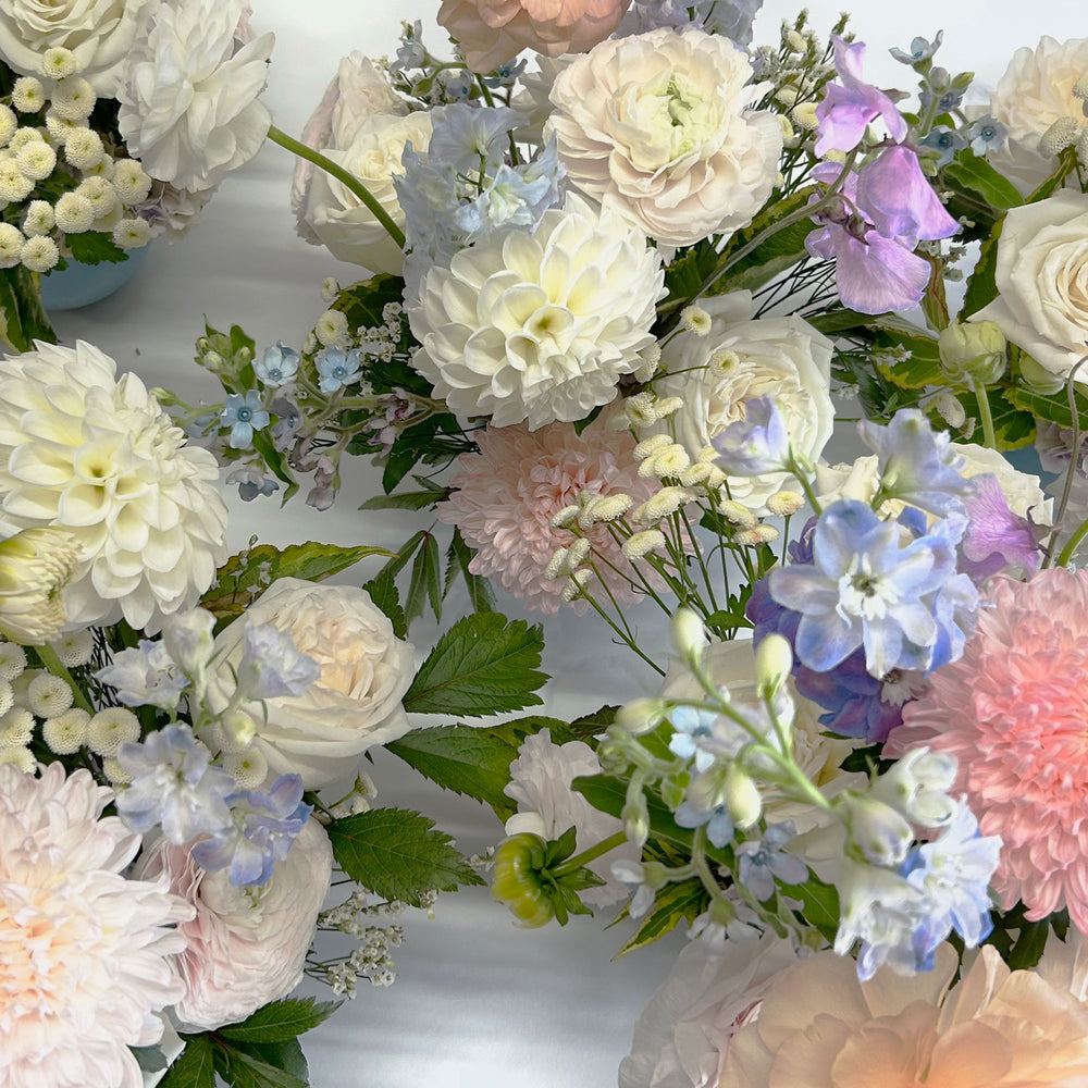 Closeup of soft white, pink and blue flowers. Bloomscape, garland, bud vases, tabletop landscape, centrepieces, deluxe garland. Our low and lush table centrepieces for round tables are designed with your colour palette and event ambiance in mind. From the best wedding florist in Toronto Quince Flowers.