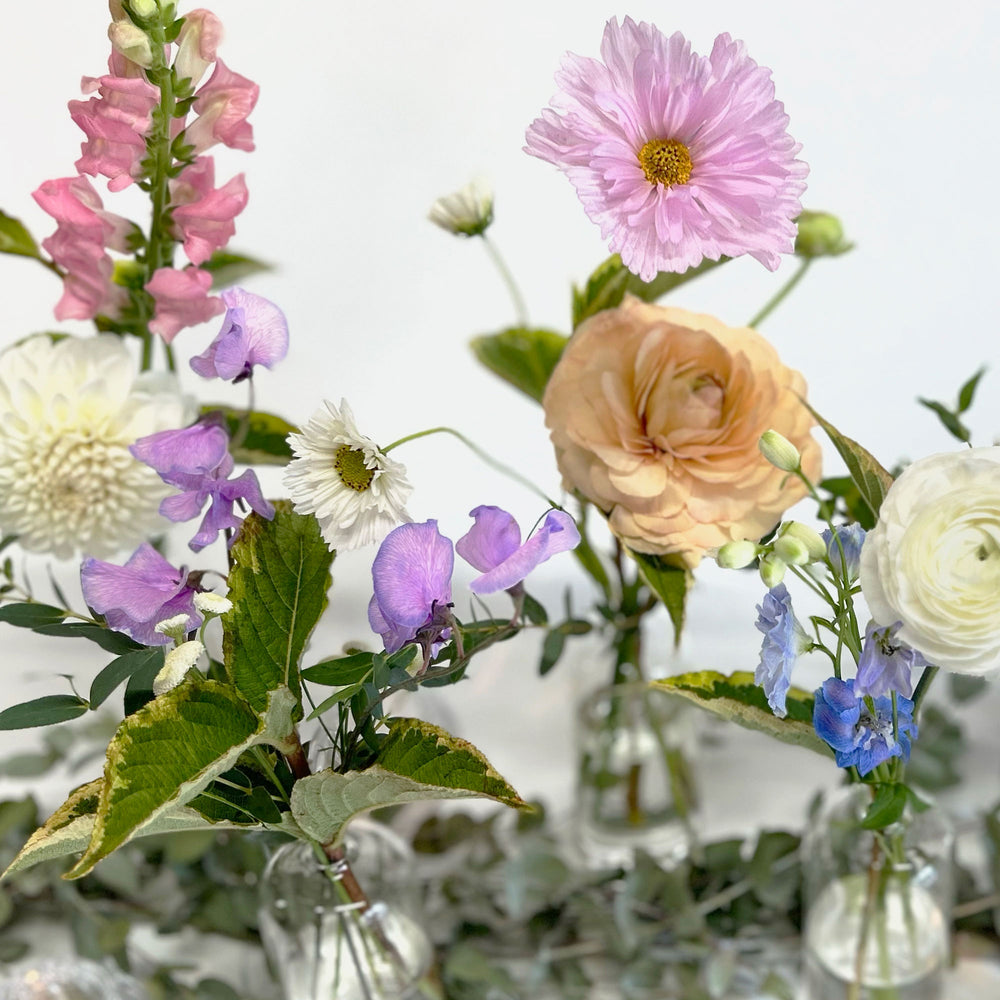 Closeup of pink, peach, white and blue flowers. Bloomscape, garland, bud vases, tabletop landscape, centrepieces, deluxe garland. Enhance your table with as many or as few "Seul Fleur" bud vases, each featuring a single focal flower and accent. Add mini arrangements to create focal points, perfect for the head table. From the best wedding florist in Toronto Quince Flowers.