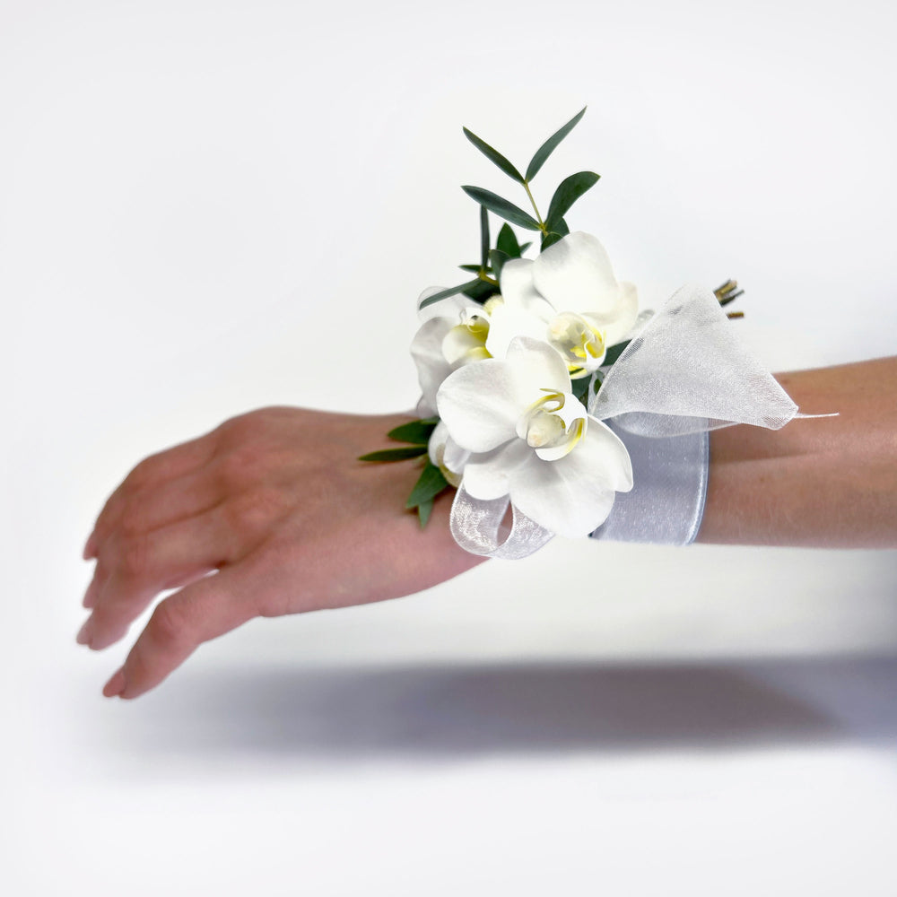 
                      
                        White orchid Corsage – It can be pinned on a woman's clothing, attached with magnets, or worn on the wrist. We like the modern look of a single large, elegant flower like an orchid bloom or garden rose. A cluster of smaller flowers also works! From the best wedding florist in Toronto Quince Flowers.
                      
                    