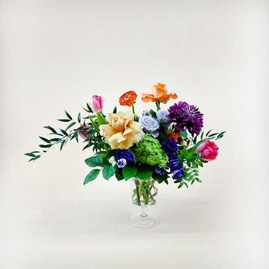 Image of a dynamic bouquet featuring yellow and lavender hues transitioning into deeper purple tones, with accents of citrus orange for vibrancy. A thoughtful and romantic combination. Order online for same-day flower delivery from Toronto's best florist, available near you.