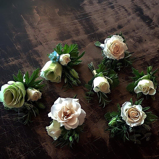 A collection of elegant floral corsage arrangements featuring white roses and green foliage on a dark, textured surface.Order online for wedding & event flowers from the best florist in Toronto near you.
