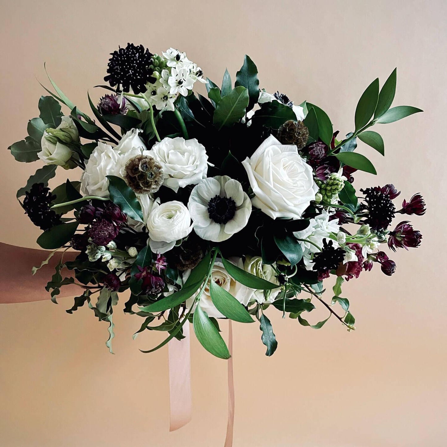 Beautiful bridal bouquet of assorted flowers including roses and poppies, adorned with a white ribbon, against a plain white background. Order online for wedding & event flowers from the best florist in Toronto near you.