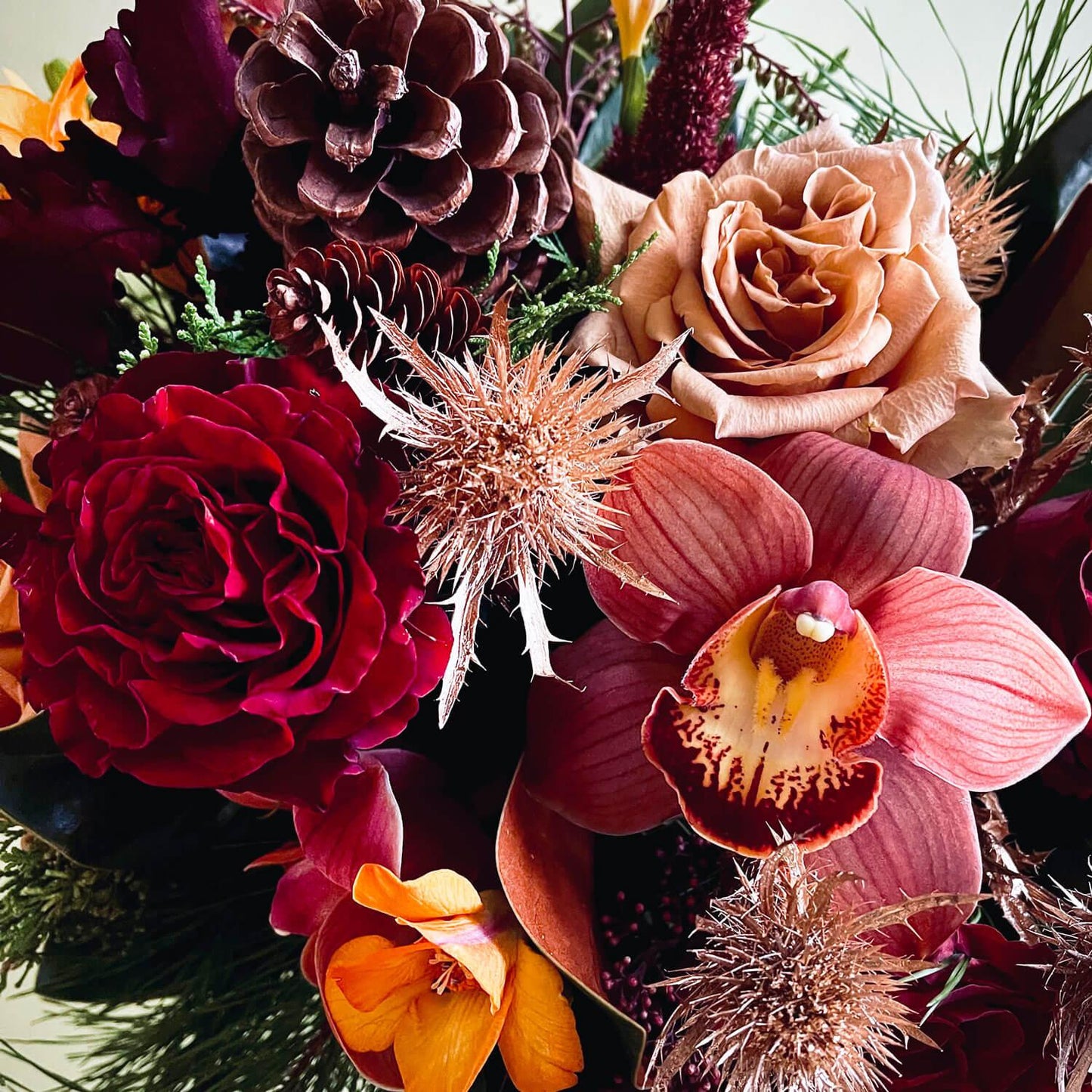 Close-up image of a celebratory bouquet featuring vivid jewel tones against deep winter evergreens and cones. Order online for same-day flower delivery from the best florist in Toronto near you.