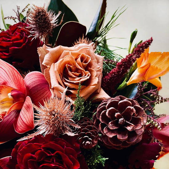 Load image into Gallery viewer, Close-up image of a celebratory bouquet featuring vivid jewel tones against deep winter evergreens and cones. Order online for same-day flower delivery from the best florist in Toronto near you.
