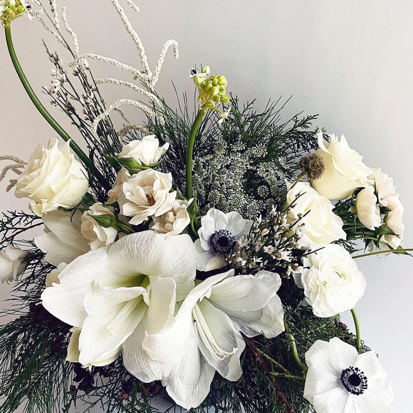 Close-up image of a bouquet featuring crisp white blooms paired with deep winter evergreens for a classic holiday look. Order online for same-day flower delivery from the best florist in Toronto near you.